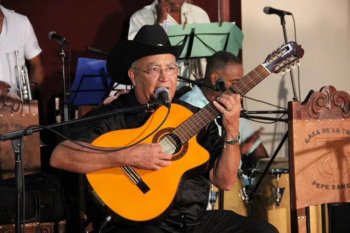 Eliades Ochoa en concert, chapeau noir, chantant au micro avec sa guitare