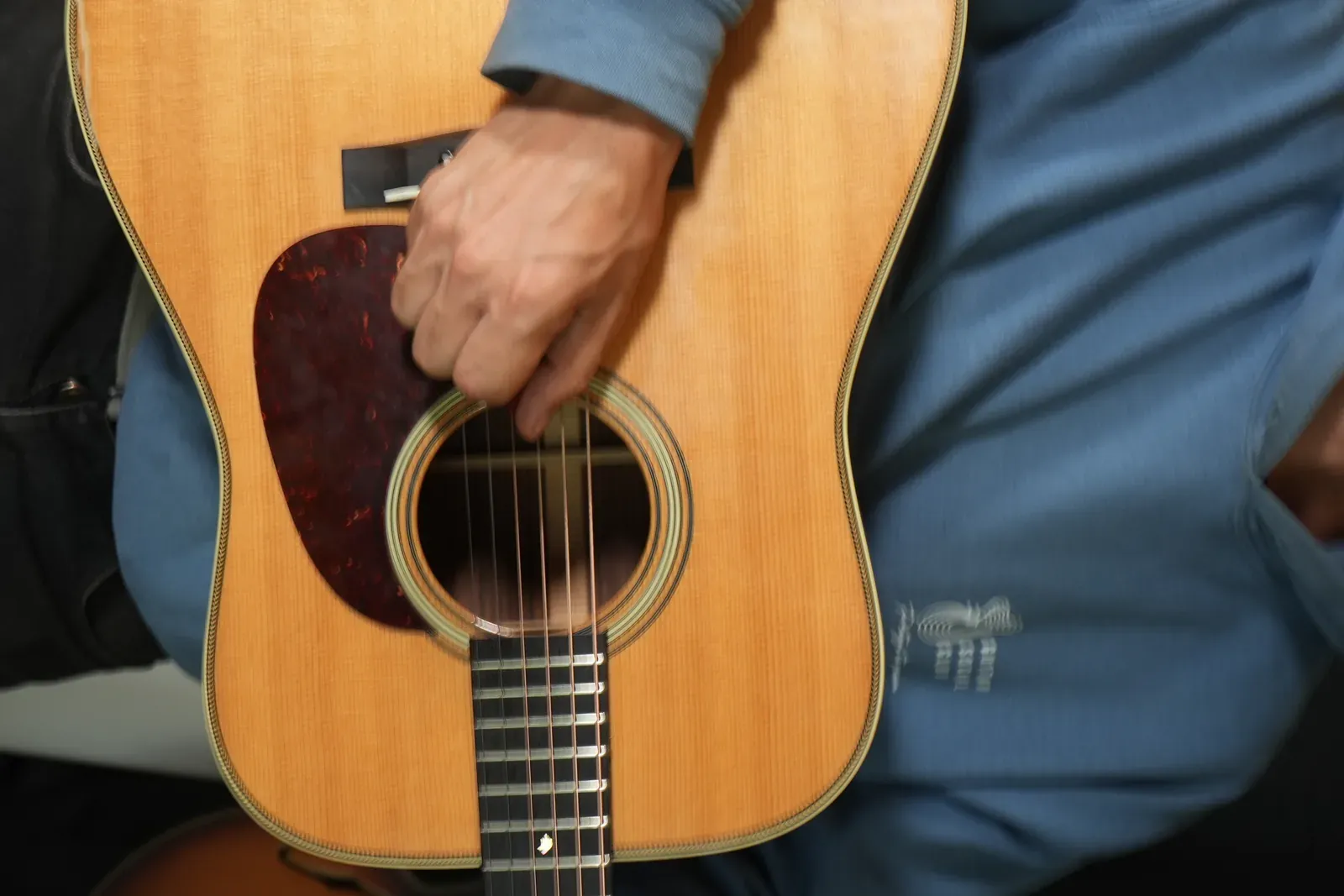 Guitariste assis dans un salon chaleureux, jouant de la guitare acoustique, bras en mouvement