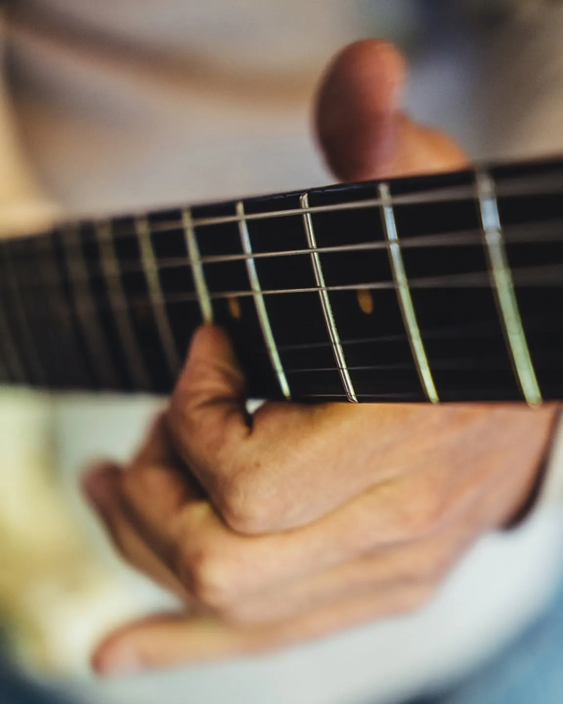 Gros plan d'une main sur le manche d'une guitare acoustique, le geste précis au cœur de la méthode Guitar Social Club