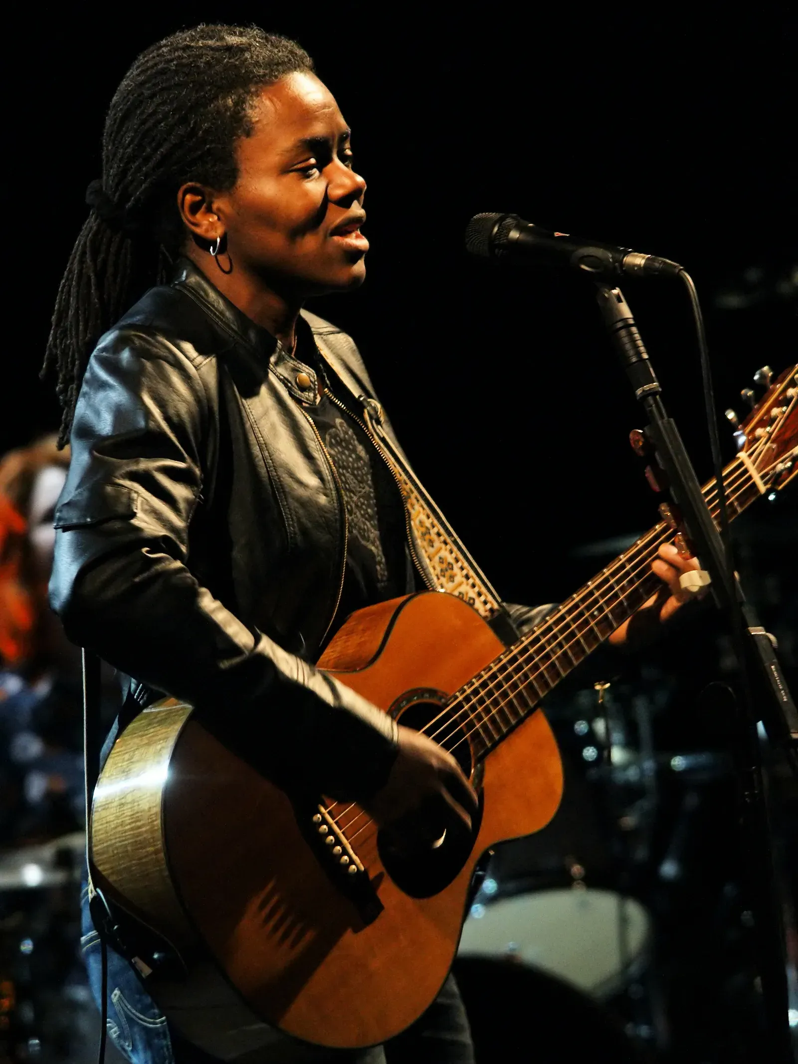 Tracy Chapman sur scène, guitare acoustique en main, devant un micro