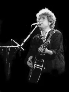 Bob Dylan en concert dans les années 70, jouant de la guitare acoustique en noir et blanc.