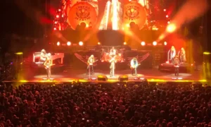 Lynyrd Skynyrd jouant en live devant une foule, sous des lumières rouges et jaunes avec le logo du groupe en fond