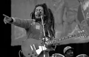 Bob Marley chantant et jouant de la guitare sur scène, en noir et blanc, le doigt pointé vers la foule