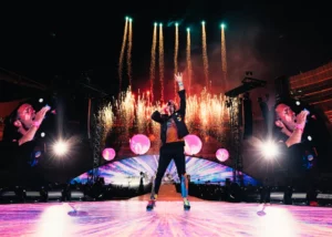 Chris Martin de Coldplay en pleine performance scénique avec feu d’artifice et jeux de lumières sur écran géant