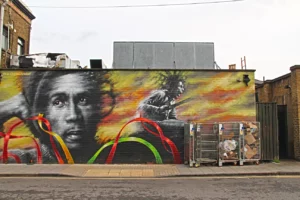 Fresque murale représentant Bob Marley avec des rubans rouges, jaunes et verts, peinte sur un mur de briques