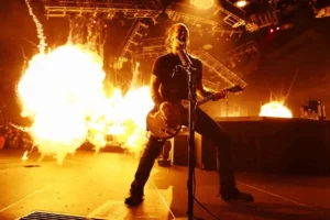 James Hetfield, chanteur et guitariste de Metallica, en concert avec des explosions pyrotechniques en arrière-plan.