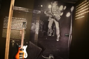 Univox Hi-Flier Sunburst de Kurt Cobain exposée dans un musée, avec une photo live du chanteur de Nirvana en concert.