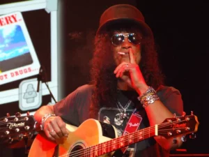 Slash jouant de la guitare acoustique avec une cigarette et des lunettes noires, en concert