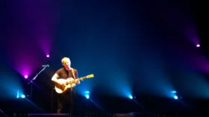 Ed Sheeran jouant de la guitare acoustique sur scène sous des lumières bleues et violettes
