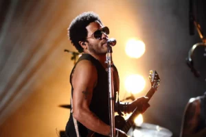 Lenny Kravitz en concert, chantant et jouant de la guitare électrique sous des projecteurs lumineux.