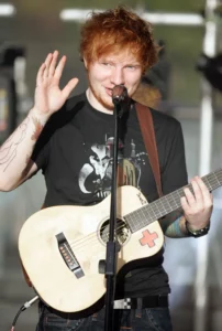 Ed Sheeran saluant le public tout en jouant de la guitare acoustique lors d’un concert, interprétant Shape of You.