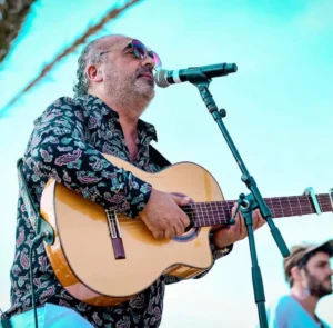 Chanteur des Gipsy Kings jouant de la guitare acoustique sur scène en plein air.